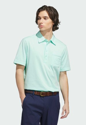 Polohemd in Minzgrün aus weichem Stoff, mit Kragen, Knopfleiste und Brusttasche. Kombiniert mit navyblauen Hosen und einem braunen Gürtel.