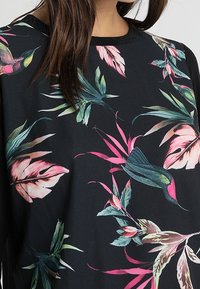 Musta toppi, jossa on eläväinen kukkakuvio vaaleanpunaisena, vihreänä ja sinisenä. Ominaisuuksiin kuuluu pyöreä pääntie ja sileä, kevyt kangas.