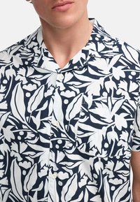 Camicia a maniche corte in cotone leggero, con un motivo floreale blu navy e bianco, colletto, bottoni e un taschino sul petto.
