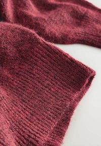 Strickpullover in einem satten Burgunderrot, mit einem strukturierten Muster in unterschiedlicher Dicke und einer weichen, fusseligen Oberfläche. Die Enden sind gerippt.