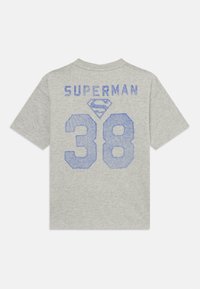 Pilkas medvilninis marškinėlis su "SUPERMAN" mėlynomis raidėmis virš numerio "38" ir mėlynu deimantu logotipu centre. Trumpomis rankovėmis, apvali apykaklė.