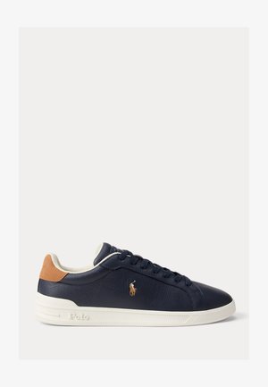 Zapatilla deportiva de cuero azul marino de corte bajo con lengüeta trasera de ante marrón, suela blanca, cordones azules marinos y logotipo bordado de Polo en el lateral.