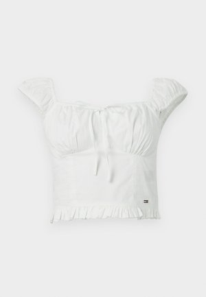 Weißes Crop-Top aus weichem Stoff, mit Puffärmel, einer gebundenen Vorderseite und einem gerafften Saum. Kleines Markenzeichen an der Seite.