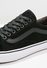 Basket noire en suede avec des lacets texturés noirs, une semelle en caoutchouc blanche et un logo sur le côté en gris avec des détails de couture contrastants.