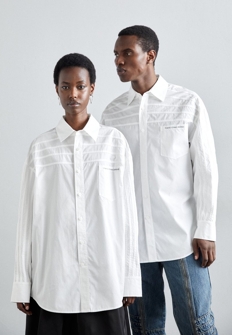 Hvite oversized skjorter med knapper har vertikale stripe detaljer og sidelommer, og de er kombinert med kontrasterende blå denimbukser.