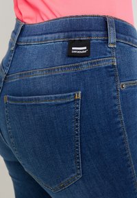 Tmavě modré džíny s přiléhavým střihem, navržené s jemnou strukturou. Mezi jejich prvky patří žluté prošití a černá etiketa s logem DRDENIM.