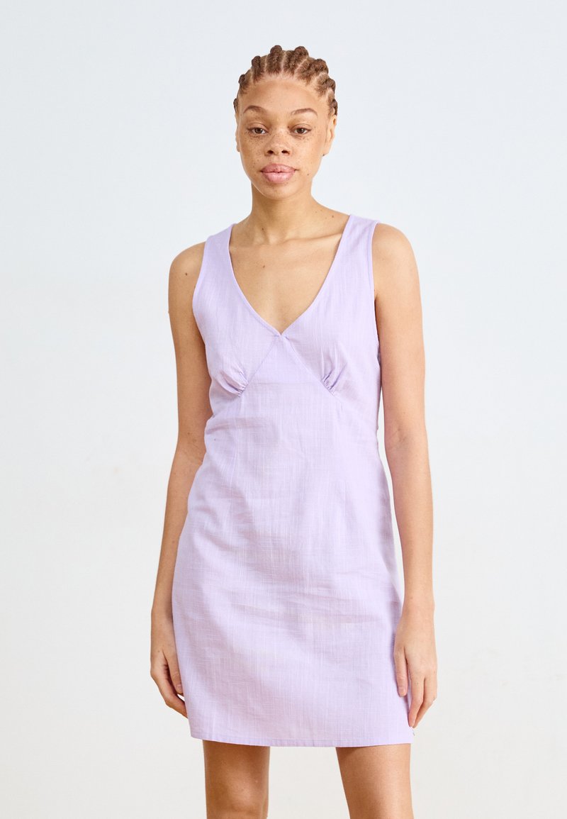 Syre lilac-värinen hihaton mekko, jossa on syvä V-pääntie, teksturoitu kangas ja ryppy yksityiskohtia rinnan alla. Yksinkertainen, muotoiltu siluetti.
