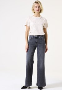 Helles rosa T-Shirt mit kurzen Ärmeln und verstreuten metallischen Sternelementen, kombiniert mit hochtaillierten, weiten, dunkelgrauen Jeans.