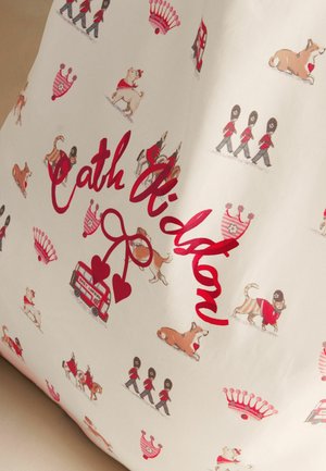 Vankúš s červeným textom "Cath Kidston," zdobený ilustráciami londýnskych strážcov, psov corgi, koruniek a dvojposchodových autobusov.