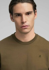 Felpa girocollo verde oliva realizzata in misto cotone, con un sottile dettaglio logo sul petto a sinistra, trama liscia e design aderente.