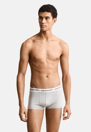 Ung mand står iført lysegrå GANT boxershorts med hvidt logo-bælte, kigger let til siden på ensfarvet baggrund.