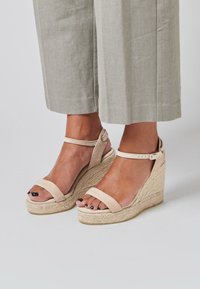 Sandales à talons compensés beiges avec une plateforme en jute tressé, dotées de deux larges bandes sur les orteils et d'une fine sangle autour de la cheville avec une boucle.