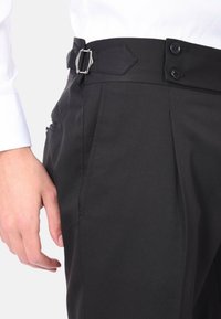 Pantaloni neri con vestibilità sartoriale, dotati di tasca laterale, chiusura con doppio bottone e una distintiva fibbia argentata con design angolato.