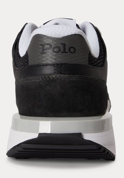 Ασημί τακούνι αθλητικού παπουτσιού σε ασπρόμαυρο με λεπτομέρειες από σουέντ και δίχτυ, λευκή επενδεδυμένη γλώσσα και λογότυπο "Polo" στην πίσω ετικέτα πάνω από λευκή σόλα.