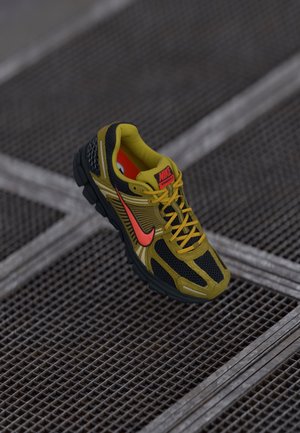 Yellow and black Nike running shoe with red swoosh and laces, placed on a metal grated surface.