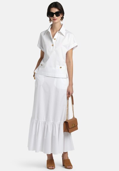 Fehér galléros blúz rövid ujjakkal és arany gombokkal, fehér, bővülő szoknyával párosítva. Barna kézitáska és barna velúr mules cipő teszi teljessé az összeállítást.