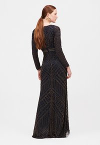 Beaded večerní šaty s dlouhými rukávy, s chevronovým vzorem v námořnické modři a zlaté, přiléhavý střih a splývavý lem.