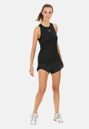 Zwarte sportieve tanktop met mouwloos ontwerp, gecombineerd met zwarte shorts. Heeft een logo op de tanktop. Model draagt zilveren sneakers.