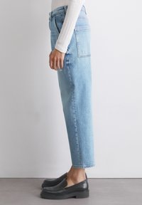 Lyseblå høyt midjede jeans med rette ben, minimal slitasje og klassisk fem-lomme-design. Kombinert med svarte slip-on sko.