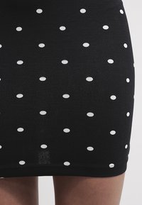 Jupe noire à pois avec un tissu extensible et lisse, ornée de points blancs circulaires uniformément espacés et d'une coupe ajustée.
