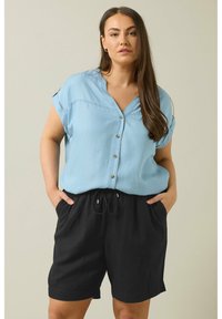 Camisa de botones de manga corta en azul claro con cuello en V y botones dorados, combinada con pantalones cortos de tiro alto negros con cordón y bolsillos laterales.