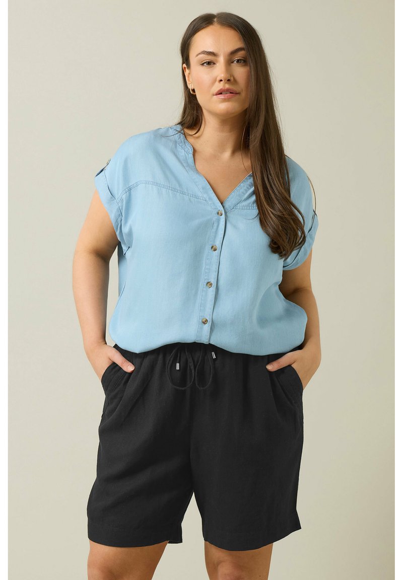 Camisa de botones de manga corta en azul claro con cuello en V y botones dorados, combinada con pantalones cortos de tiro alto negros con cordón y bolsillos laterales.