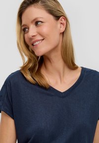 Granatowy t-shirt z dekoltem w serek, wykonany z miękkiego materiału, z krótkimi rękawami i subtelnymi detalami na ramionach. Gładka tekstura i luźny krój.