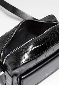 Svart lädercrossbodyväska med en texturerad krokodilåttning, silverdragkedja, öppet topp och en varumärkesdetalj vid basen.