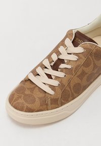 Pruunide mustriga sneakerid tekstuurse kangast ülemise osaga, kreemjatest nööridest ja heledast kummist tallast. Ülemisel osal on pruun logo detail.