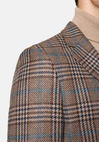 Brązowa marynarka w kratę z niebieskimi i ciemnobrązowymi akcentami, wykonana z teksturowanej tkaniny, z ostrym kołnierzem i dopasowanym krojem.