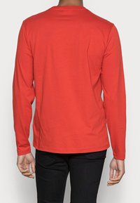Maglietta a maniche lunghe rossa con collo rotondo, realizzata in cotone morbido. Il design presenta una linea dritta e linee semplici e pulite.