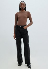 Braunes, geripptes Langarmshirt, kombiniert mit hoch-taillierten, dunklen Denim-Jeans. Die Jeans haben einen geraden Schnitt und Vordertaschen. Schwarze Knöchelstiefel.