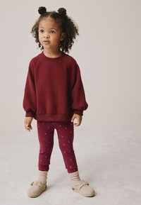 Burgundski pulover z napihnjenimi rokavi, kombiniran z burgundskimi legicami z majhnim cvetličnim vzorcem in bež natikači.