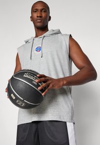 Pelēks bez piedurknēm, ar zilu un sarkanu basketbola logo, apvienots ar melnajām acs šortiem. Cilvēks tur melnu basketbola bumbu.