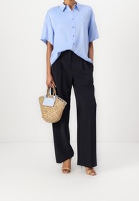 Světlomodrá košile na knoflíky, černé kalhoty s vysokým pasem a pletená ratanová kabelka se světlomodrým detailem. Celkový vzhled doplňují béžové sandály.