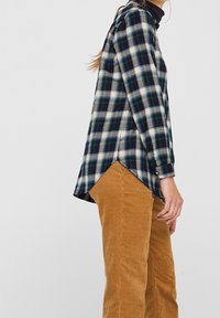 Camicia a maniche lunghe a quadri con check blu, verde e bianco, con orlo curvo. Abbinata a pantaloni in corduroy marroni texture.