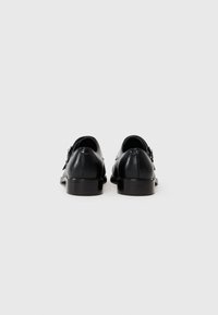 Black leather shoes with a smooth finish, featuring a rounded toe, low stacked heel, and decorative buckle detail on each side.