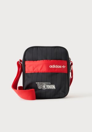 Schwarze und rote Adidas Umhängetasche mit verstellbarem rotem Gurt, Adidas-Logo und 1. FC Union Berlin Schriftzug sowie Emblem auf der Vorderseite.