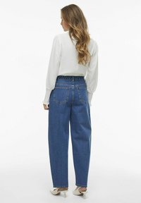 Zila džinsu bikses ar augstu jostasvietu un taisnēm kājām, ar teksturētu apdari. Balts garām piedurknēm tops, bēšas augstpapēžu kurpes, vienkāršs dizains.