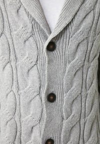 Grå stickad kofta med ett kabelstickat mönster, sjalkrage och fyra mörkbruna knappar framtill.