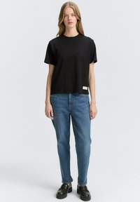 Zwart t-shirt met korte mouwen en een ronde hals, gecombineerd met blauwe recht gesneden jeans. Heeft een klein merkembleem aan de zoom.