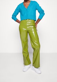 Cárdigan de punto turquesa con escote en V, combinado con pantalones de vinilo verdes lima brillantes y zapatillas blancas. Colores brillantes con texturas suaves.