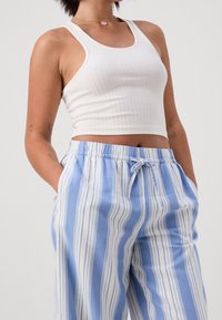 Ribbad vit crop-top med tjocka band, kombinerad med ljusblå randiga vida byxor med dragsko i midjan och sidfickor.