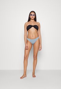 Top de biquíni preto sem alças com tecido texturizado e detalhe em nó; parte de baixo de biquíni azul claro às riscas com aberturas altas nas pernas.