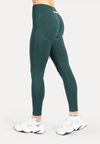 Ciemnozielone legginsy z wysokim stanem z teksturowanym wzorem i dopasowanym krojem. W zestawie białe buty sportowe z czarną podeszwą.