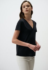 Czarny t-shirt w kształcie v-neck wykonany z lekkiego materiału, z krótkimi rękawami i luźnym krojem, w połączeniu z jasnymi, dopasowanymi spodniami.