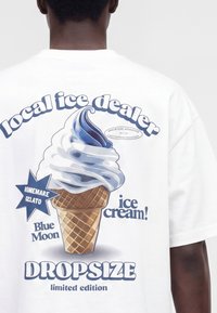 Homme portant une chemise blanche avec un graphique de cornet de glace bleu et blanc et texte indiquant vendeur local de glace, gelato maison, Blue Moon, édition limitée dropsize.