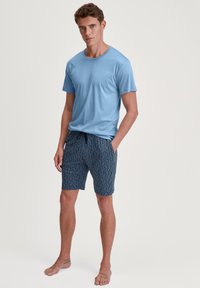 Lichtblauwe t-shirt met korte mouwen in combinatie met marineblauwe shorts met een golvend wit geometrisch patroon. Het materiaal lijkt zacht; de shorts hebben een elastische tailleband.