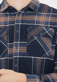 Marine flanellen shirt met een tan en witte ruitpatroon, voorzien van een button-down kraag, twee borstzakken en blauwe knopen. Zachte textuur.