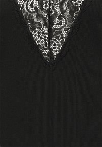 Top preto com textura canelada, apresentando um decote em V adornado com intrincada renda preta e uma borda recortada.